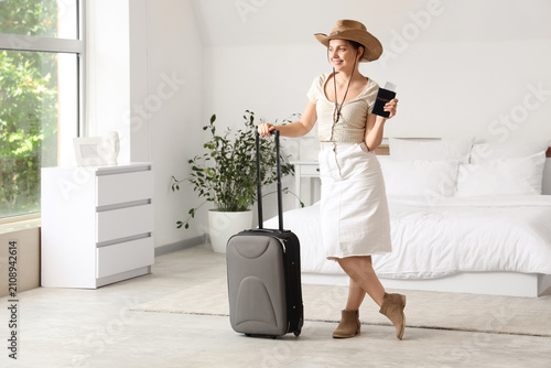 Young woman in a straw hat holding a passport and pulling a suitcase, ready f...