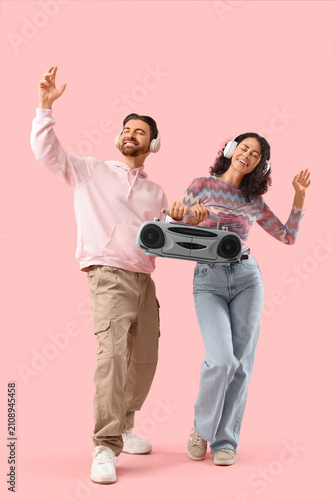 Fotografie Young couple in headphones with boombox dancing on pink background