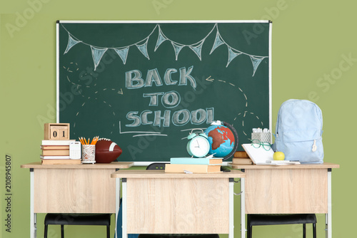 Blackboard with text BACK TO SCHOOL and desks in classroom