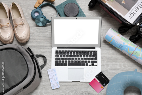 Blank laptop with credit cards and travel accessories on grey wooden floor
