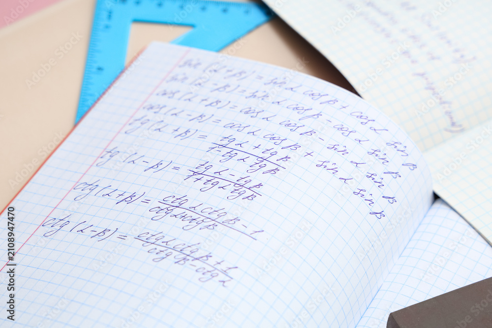 Obraz premium Open copybook with maths formulas and ruler on color table, closeup