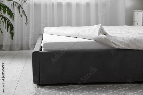 фотографія New orthopedic mattress with blanket on stylish bed in room, closeup