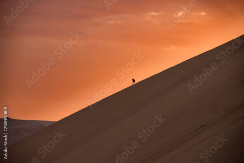Solo traveler silhouette ascend vast desert dune at sunset in Peru