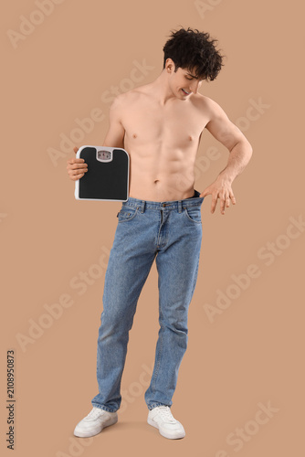 Foto Handsome young happy sporty man in loose jeans with scales on brown background