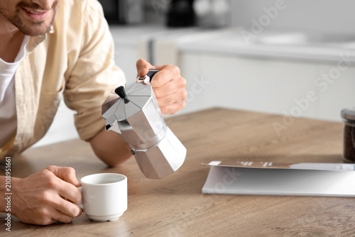 Man pouring espresso from geyser coffee maker into cup in kitchen, closeup