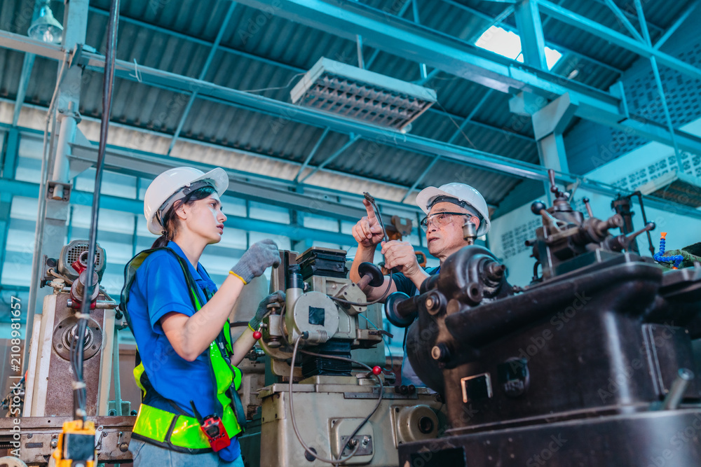 Fototapeta premium Senior Male Engineer Teaches Young Woman Technician to Operate Machinery in Industrial Factory
