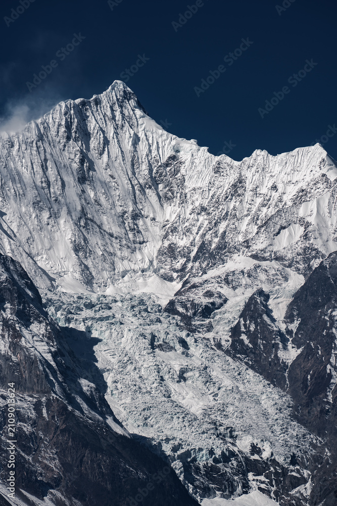 Naklejka premium Steep Snow-capped Mountain Ridge and Giant Valley Glacier, Raw Alpine Mountain Texture Under Deep Blue Sky