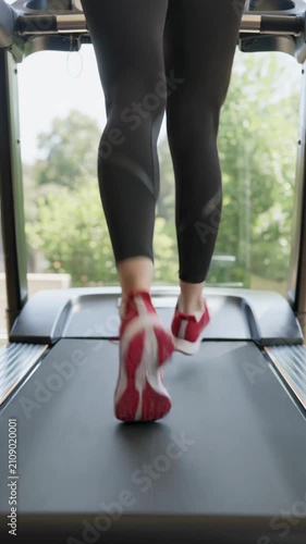 Close-up of legs running on treadmill in gym, vertical shot