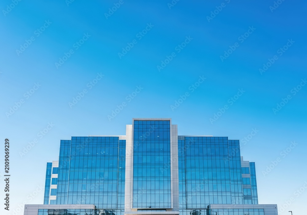 Fototapeta premium A contemporary healthcare facility featuring a polished glass facade reflects the bright sunshine beneath a wide and cloudless blue sky, windows, healthcare, urban