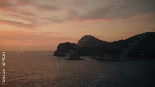 Sweeping aerial footage captures Es Vedrá island and Cala d'Hort’s rugged coastline at golden hour, with tranquil waters, dramatic silhouettes, and vibrant, colorful sunset skies.