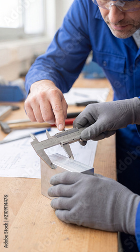 Industrial worker using vernier caliper on metal block