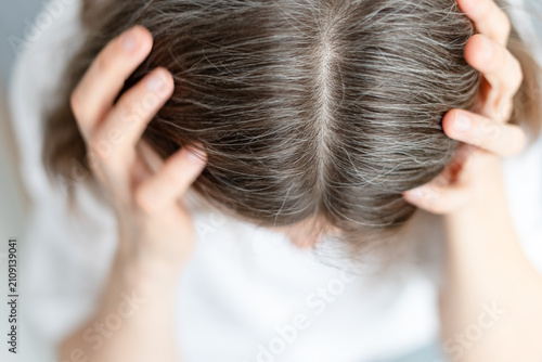 Close up of a woman gray hair that resulted from severe chronic stress in her life. The mature adult recognizes how emotional trauma caused silver strands. Mother sees her anxiety written in gray.