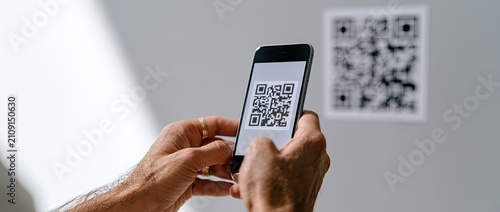 Person scanning a QR code on a wall with a smartphone.