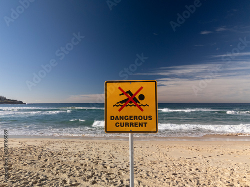 No swimming dangerous current sign at beach on perfect sunny day with blue sky and waves.