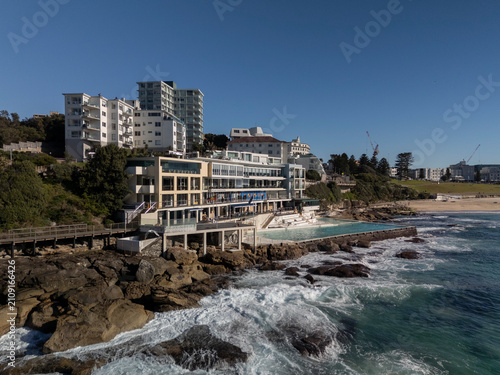 Bondi Beach on beautiful sunny day with blue sky looking to Icebergs pool, skyline and beachside architecture.