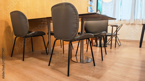 A minimalist dining area features a sleek table surrounded by stylish Grey leather chairs and wooden tables interior set in minimalist cafe showcasing contemporary design in a warm, inviting space.