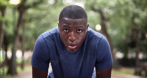 Tired, portrait and man on break, fitness and breathing after physical activity or exhausted at park. Runner, fatigue and workout recovery in nature, rest and black person with sweat and wellness