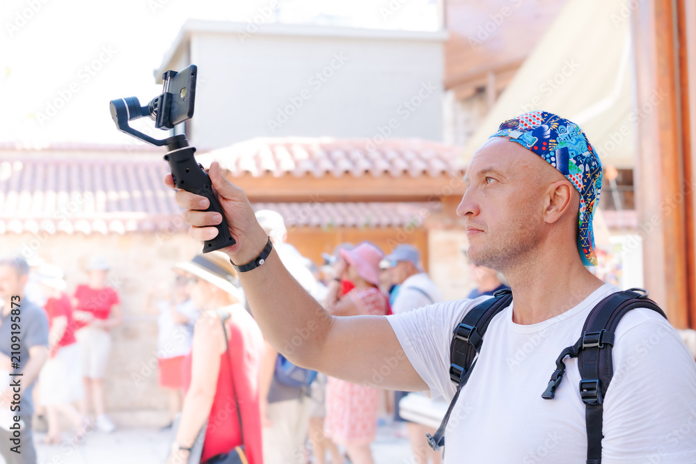 Fototapeta premium Bald Man Films with Smartphone Gimbal at Crowded Tourist Street Kaleici