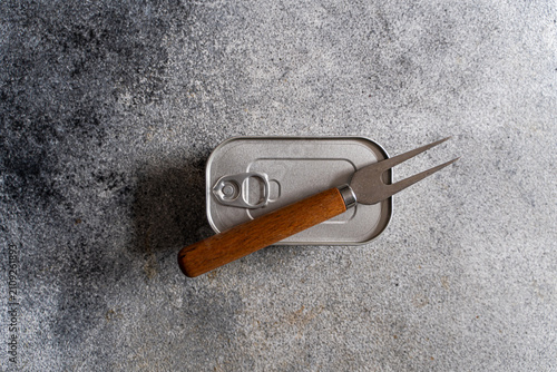 Close-up overhead view of an unopened tin of canned fish and a fork on a concrete worktop