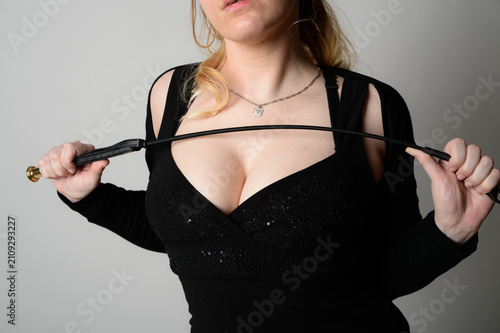 Porträt einer jungen erwachsenen Frau in elegantem schwarzen Kleid mit dekorativem Band. Stilvolle Modeaufnahme mit modernem Fashion-Look im Studio und minimalistischer Beleuchtung. bdsm peitsche domi