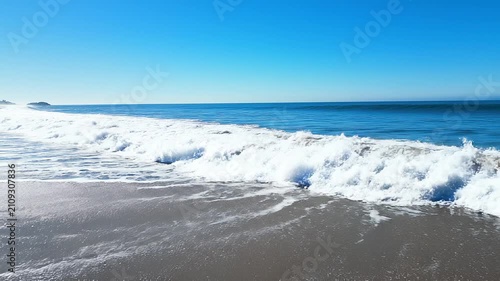 Big blue ocean waves crashing onto a pristine white sand beach along the California Pacific Coast near Los Angeles during a bright summer afternoon.