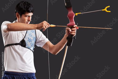 Konstfotografi Man aiming bow and arrow isolated over black background