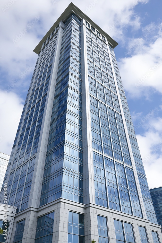 Obraz premium Modern Glass Skyscraper Reflecting Blue Sky and Clouds, Symbolizing Business and Urban Architecture