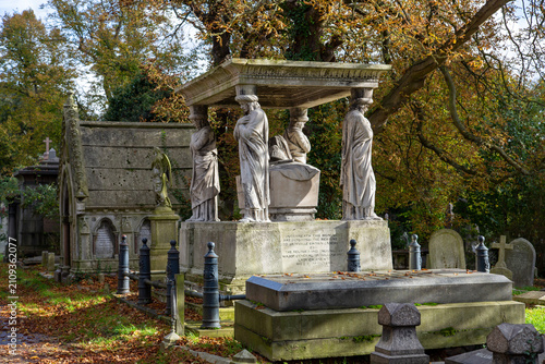 Foto Caryatids on a Victorian stone memorial among autumnal trees and gravestones in