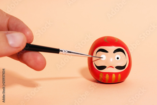 Hand of person painting details of traditional Japanese Daruma doll