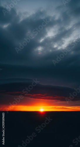 A dramatic sky where dark storm clouds gather over a vast flat landscape during sunset, creating a powerful contrast at the distant edge, panoramic, clouds, landscape