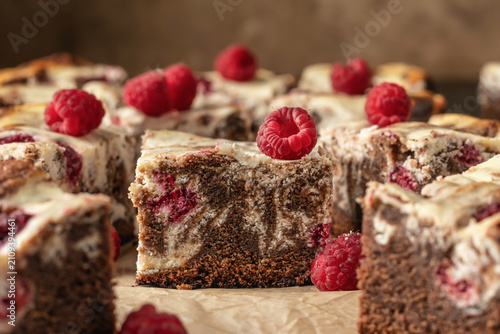 Chocolate brownies with raspberries and cream cheese swirls on baking parchment sheet, dark brown background. Cheesecake brownies