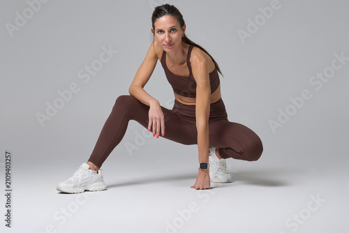 Athletic woman crouching in brown fitness outfit looking at camera in studio
