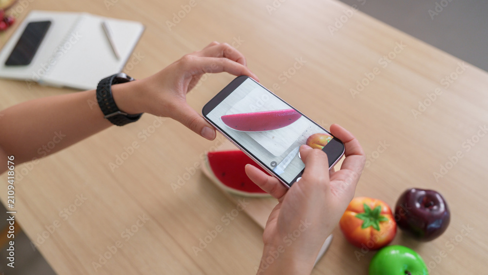 Obraz premium Cropped hands holding smartphone to take photo of toy watermelon on table