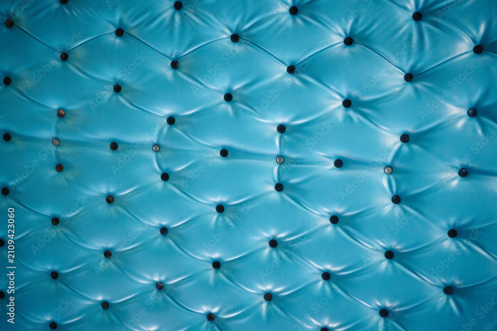 Obraz premium Close-up of a vibrant blue tufted leather surface with button details, showcasing a diamond pattern and glossy texture.
