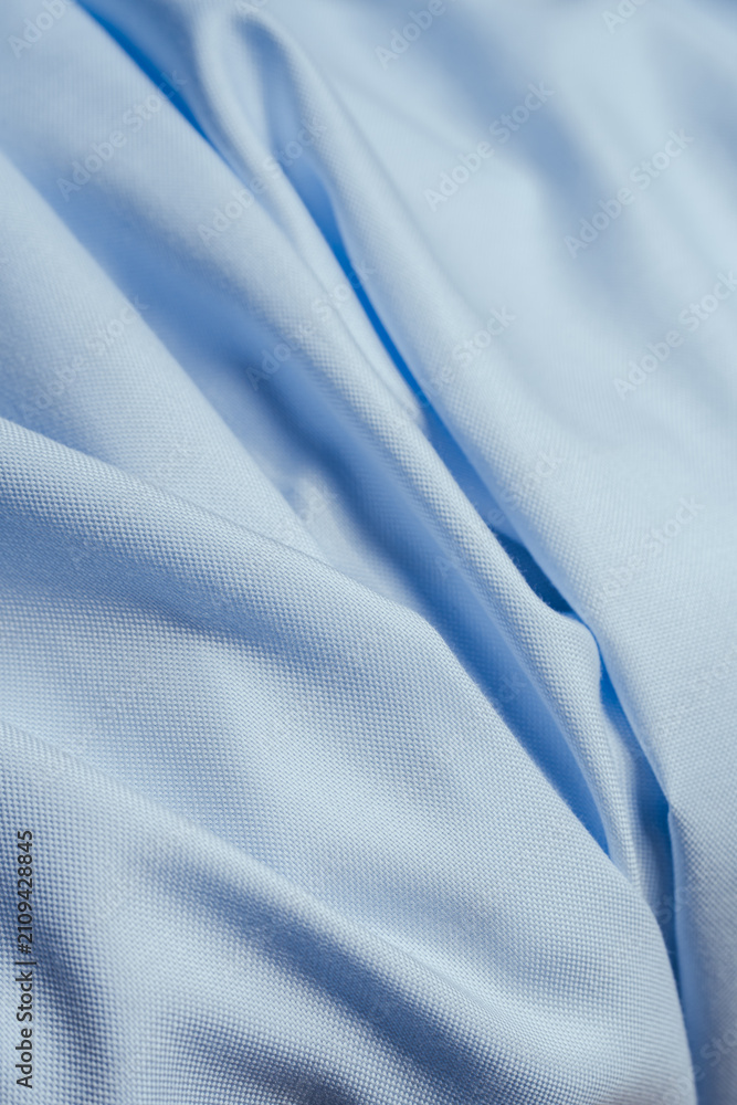 Fototapeta premium Close-up of soft light blue cotton fabric with natural folds creating an elegant textile background.