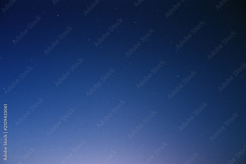 Fototapeta premium The Starry Night Sky Over a Quiet Horizon With Soft Blue Glow