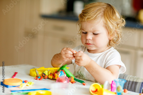 Adorable cute little toddler girl with colorful clay at home. Healthy baby playing and creating toys from play dough at nursery or playschool. Small kid molding modeling clay, creative activity