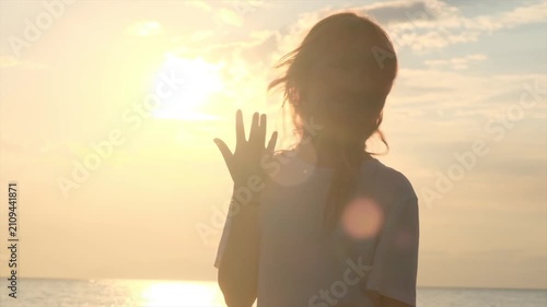 Teenage girl on the seashore at sunset performs the popular Six Seven hand gesture. Cute playful teenager follows internet trends and memes, cheerful young person, social media culture.