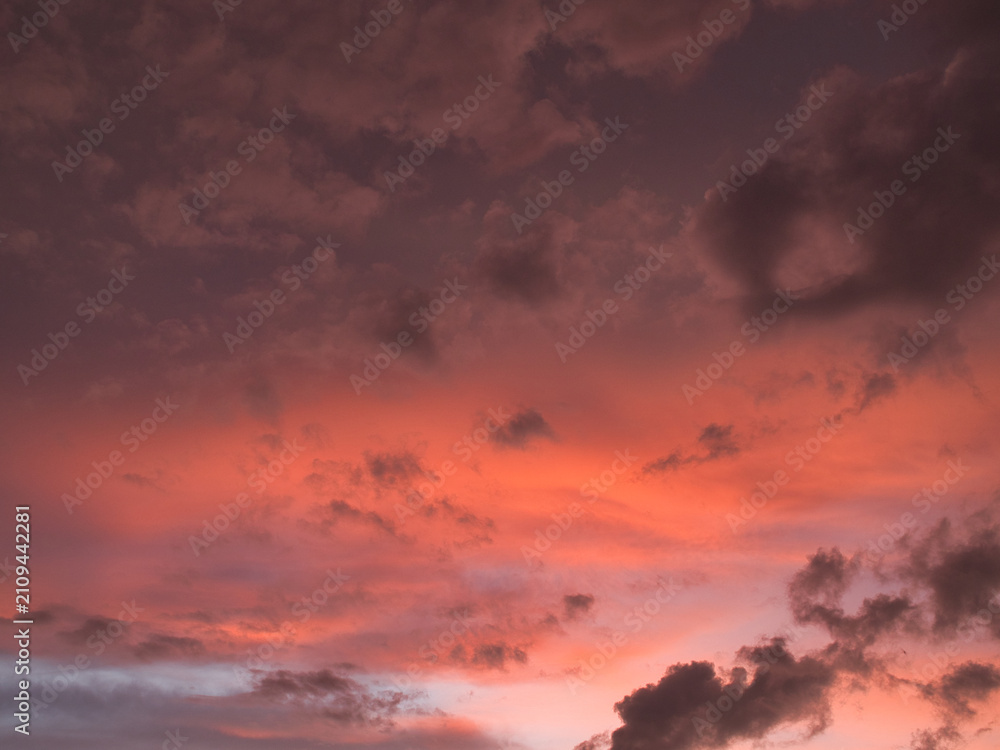 Fototapeta premium Sunset featuring deep red and orange hues contrasting with dark-textured clouds suitable for a wallpaper or background.