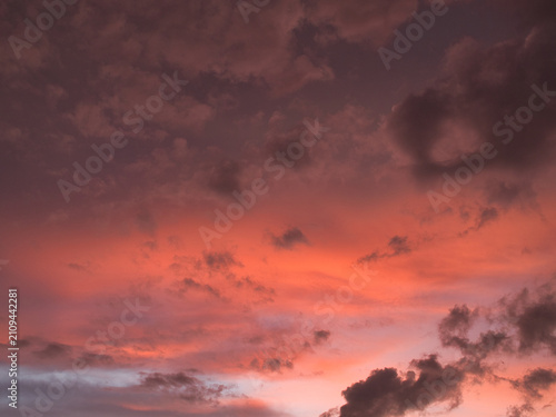 Sunset featuring deep red and orange hues contrasting with dark-textured clouds suitable for a wallpaper or background.