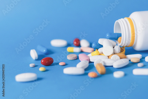 Fotografie Assorted Pharmaceutical Pills Spilled from Bottle on Blue Surface