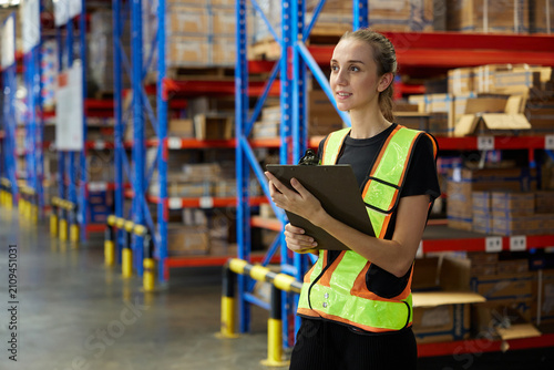 Warehouse worker checks a clipboard while standing in a well-organized storage facility in a warehouse