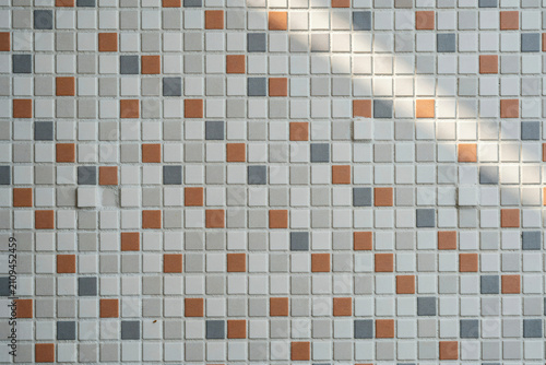 A close up view of a square mosaic wall tile pattern featuring a mix of white, light grey, and terracotta orange colored small tiles