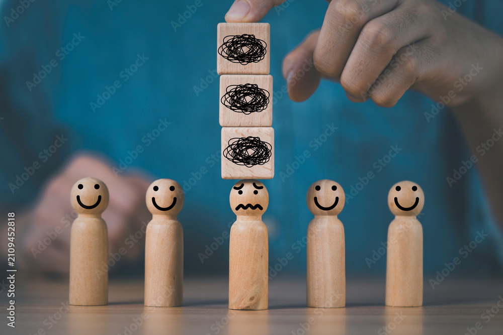 Naklejka premium Stress concept with wooden figures as a hand stacks burden blocks above one person, representing mental pressure, workplace stress, emotional overload, burnout, anxiety and employee wellbeing.