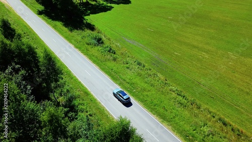 Foto Single car navigating down a scenic country road surrounded by lush green fields
