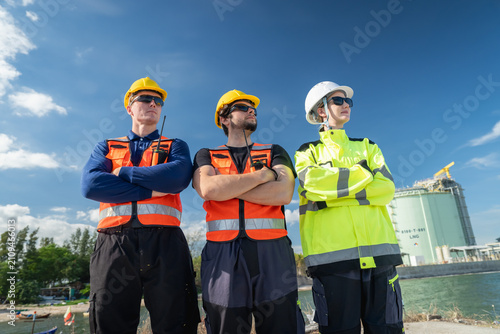 Three construction workers wearing safety gear standing proudly under a clear blue sky