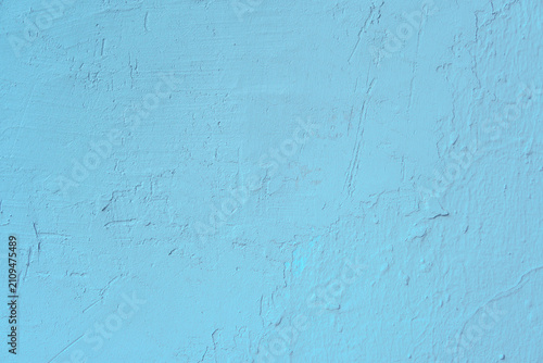 Light blue painted stucco wall with uneven surface reliefs and fine vertical cracks. Minimalist sky-colored background featuring weathered cement masonry details and industrial grunge characteristics.