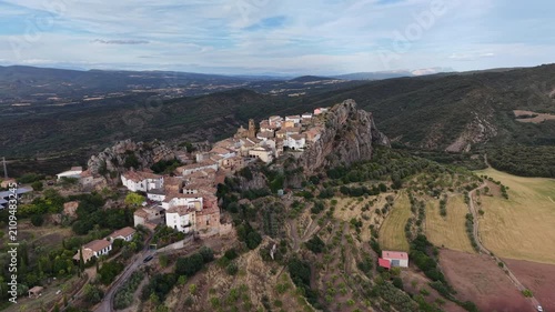 Aerial of a scenic Spanish village in the Pyrenees, located on the top of a rocky mountain. Dolly shot of village with typical olive groves and pastures in the valley below.