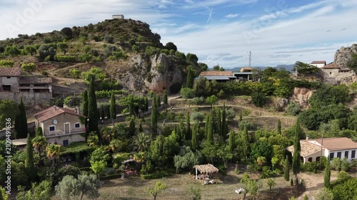 Aerial shot of beautiful garden and houses in a scenic Spanish village in the Pyrenees. Camera approaches and rises to reveal vast landscape behind mountain.