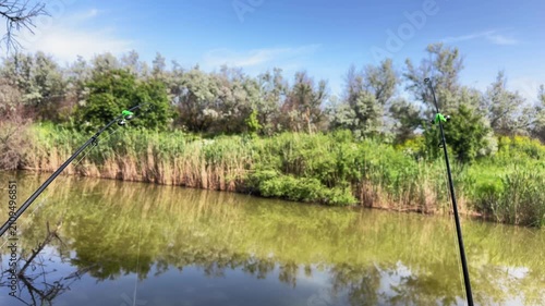 Fishing rods standing near water during fishing session at lake. Concept of sport fishing and outdoor recreation.